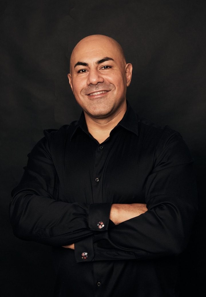 Behind the Build | Insights from Babak Nikraftar 1 Confident professional man in black shirt with arms crossed, smiling, against dark background, representing IsleFlow Content Studio Inc. It is Babak Nikraftar founder of Condoworks Transformations and Forte Projects